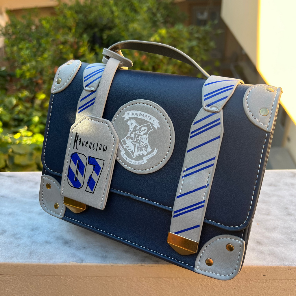 Blue handbag with a brand logo and strap details on a wooden surface.